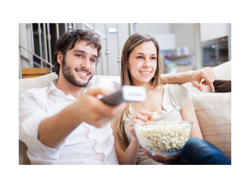 A couple sitting on the couch with popcorn watching tv